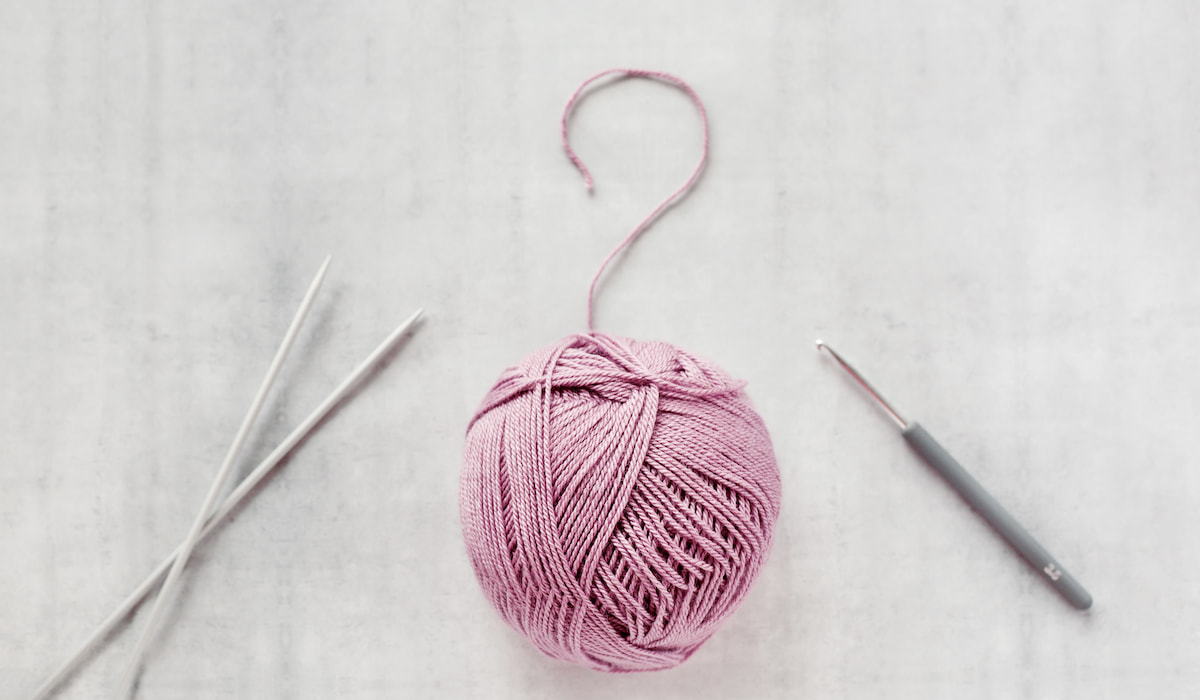 Ball of yarn, crochet hook and knitting needles on white background