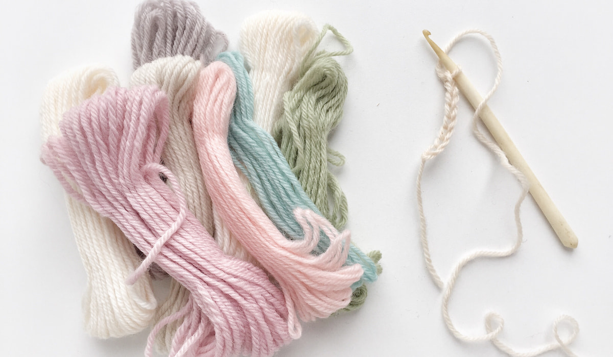 Pastel colored yarn and a crochet hook on white background