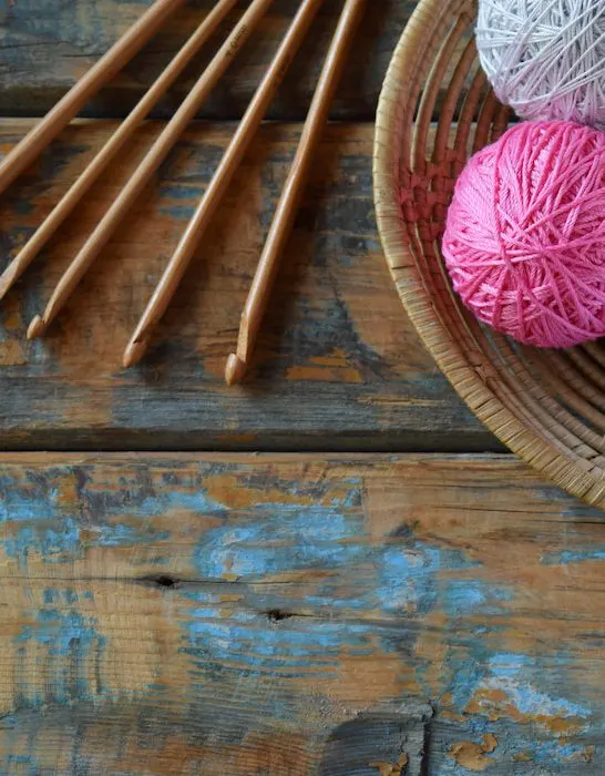 wooden crochet hooks and woolen balls in a basket