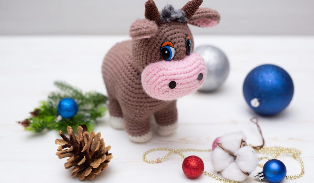 A knitted bull toy with Christmas decoration on white table