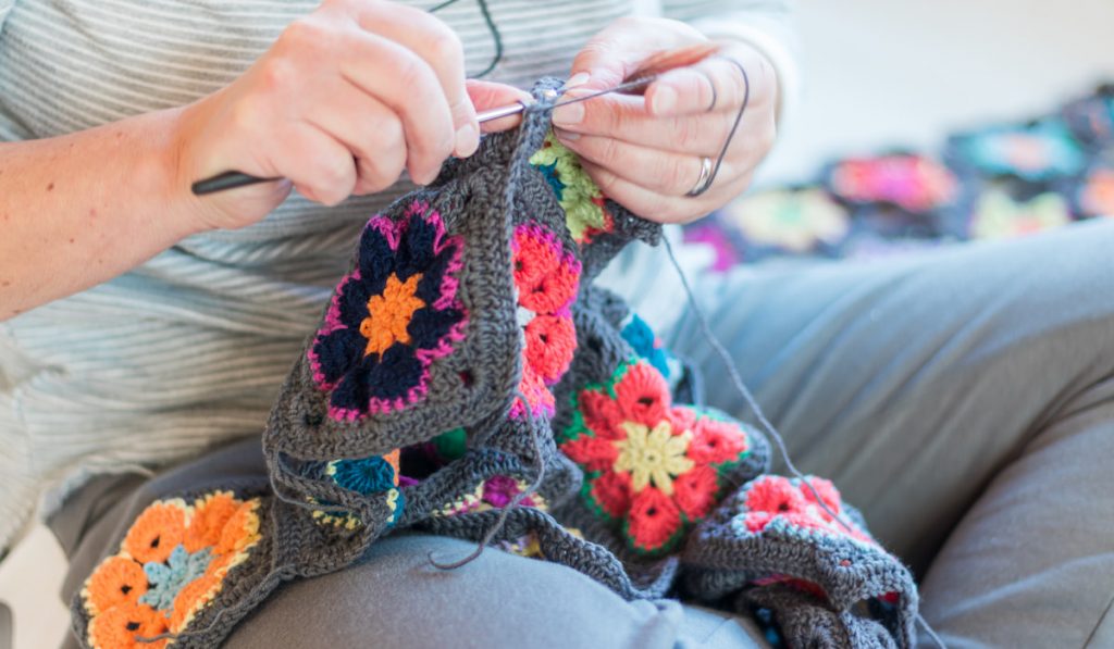 A woman sits on the floor and knits with a crochet and thread
