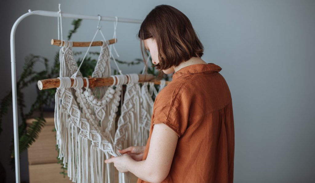 A young girl weaves macrame panels at home
