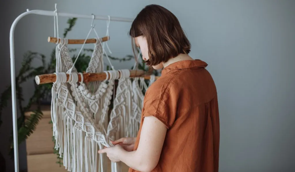 A young girl weaves macrame panels at home