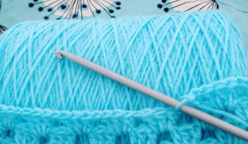 Blue crochet, plastic hook and wool on blue background 