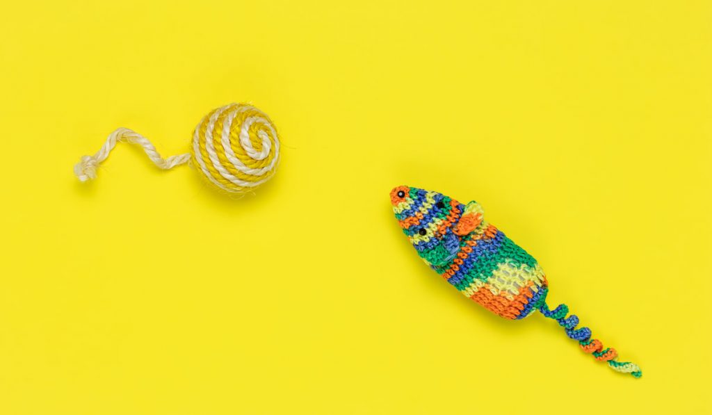 Colorful croheted mouse toy and crocheted ball on yellow background