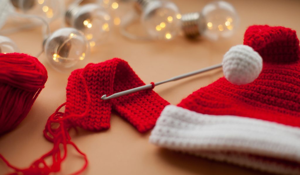 Crochet hook, red and white crochet santa hat and christmas lights and red yarn 