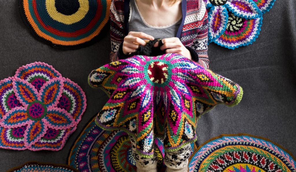 Cropped view of woman sitting on floor crocheting, surrounded by crochet circles
