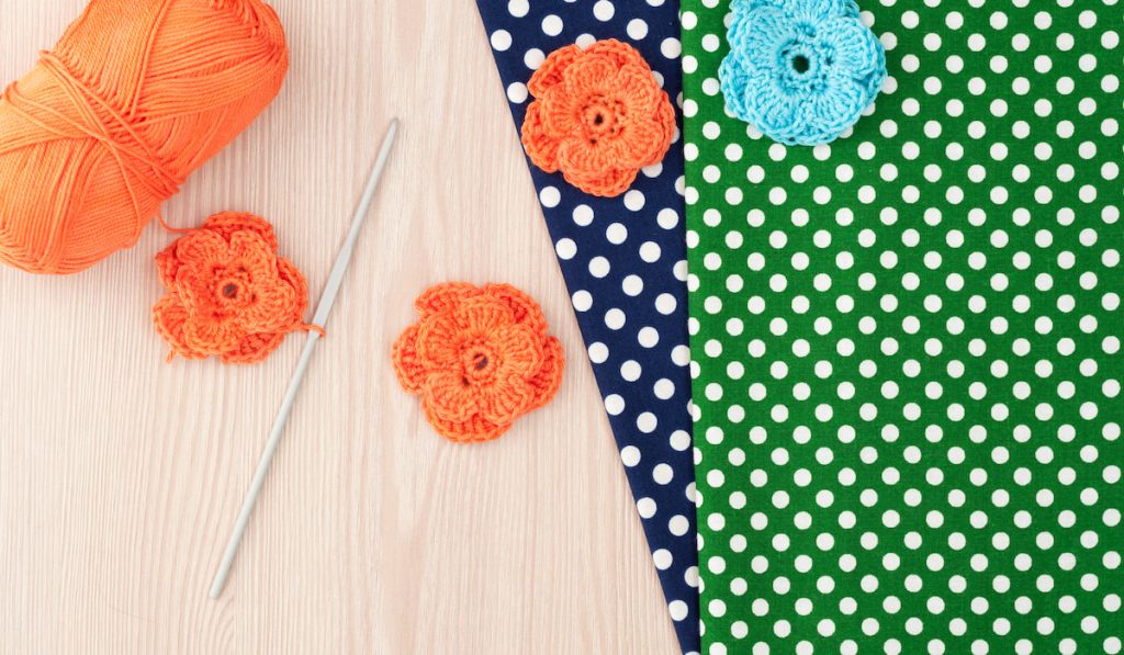 Handmade knitted crochet flowers,hook and colorful fabric on table