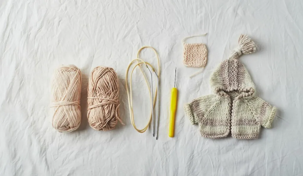 Handmade knitted small sweaters and threads on light background