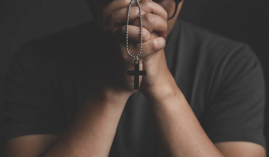  Man praying holding a cross on black background 
