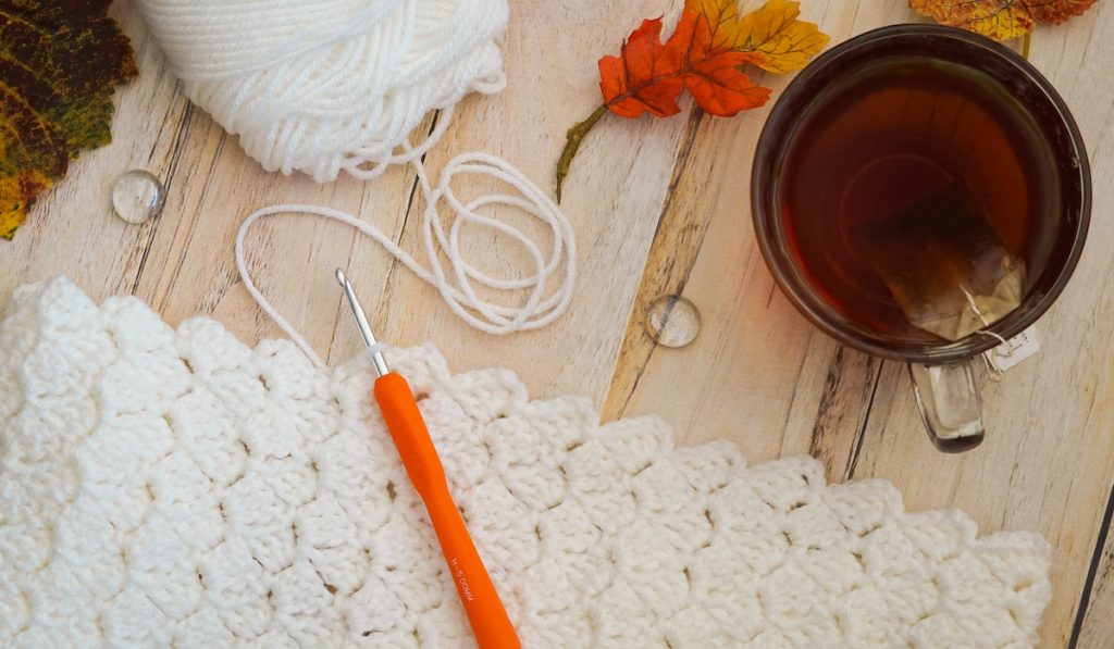 Overhead view of a crochet project with cup of tea on wooden table