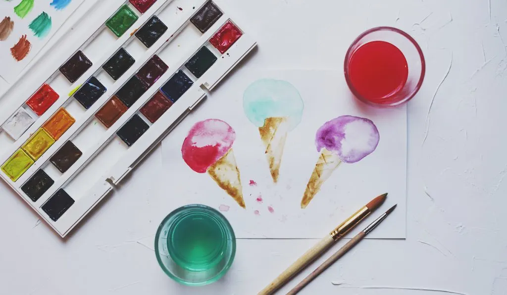 Palette of watercolor paints and glass of water on the table 