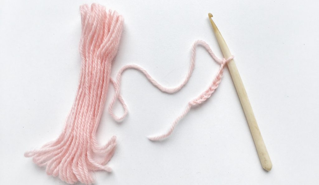 Pink yarn and a crochet hook on white background 
