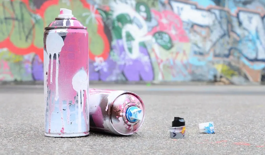 Several used spray cans with pink and white paint and caps for spraying paint