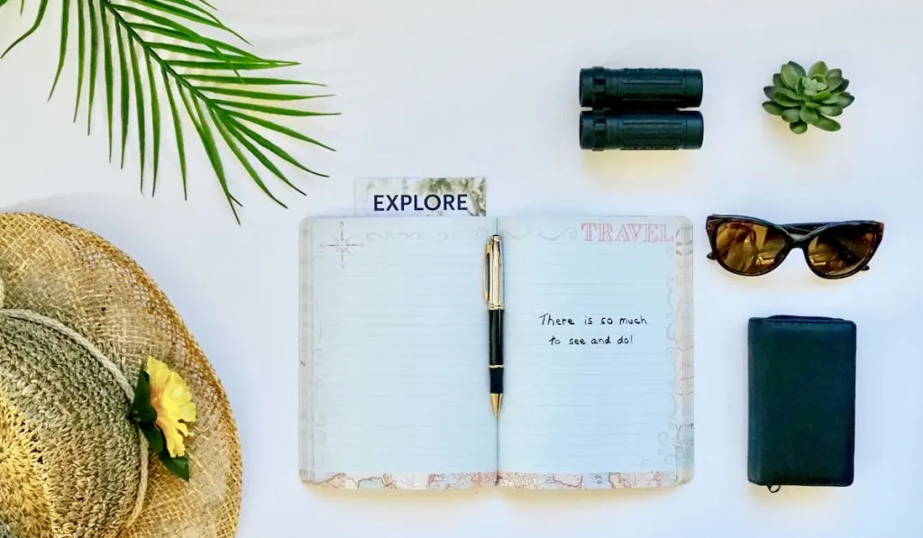 Travel flatlay items journal sunglasses binoculars hat