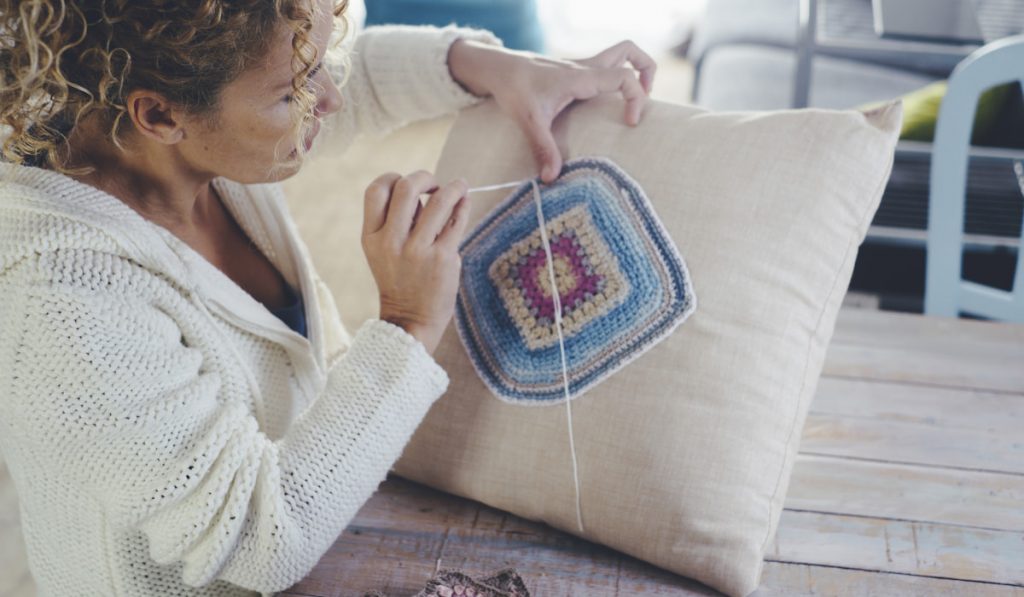 Woman at home doing crochet on a white pillow to decorate and produce decorations