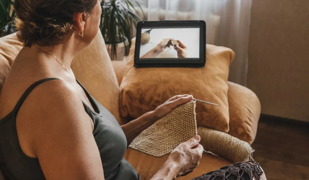 Woman crochets napkin at home watching pattern online 