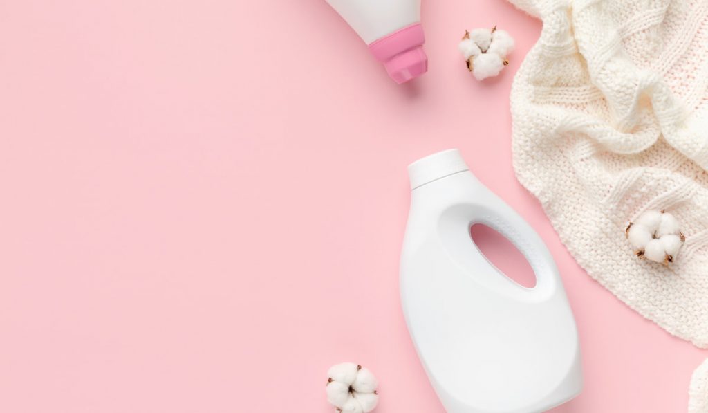 Wool sweater with cotton flower detergent bottle on pink background 