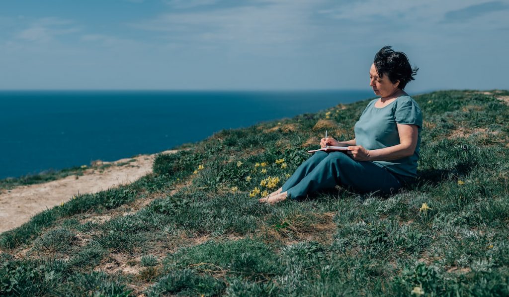 adult woman peacfully writing on her journal bear the sea