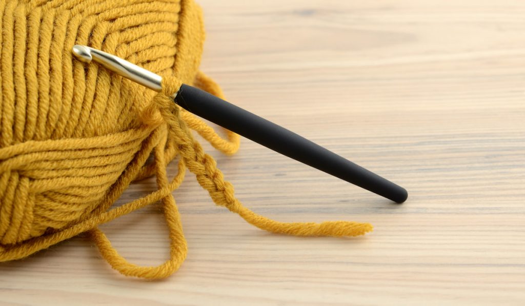 crochet hook and yellow wool on wooden table