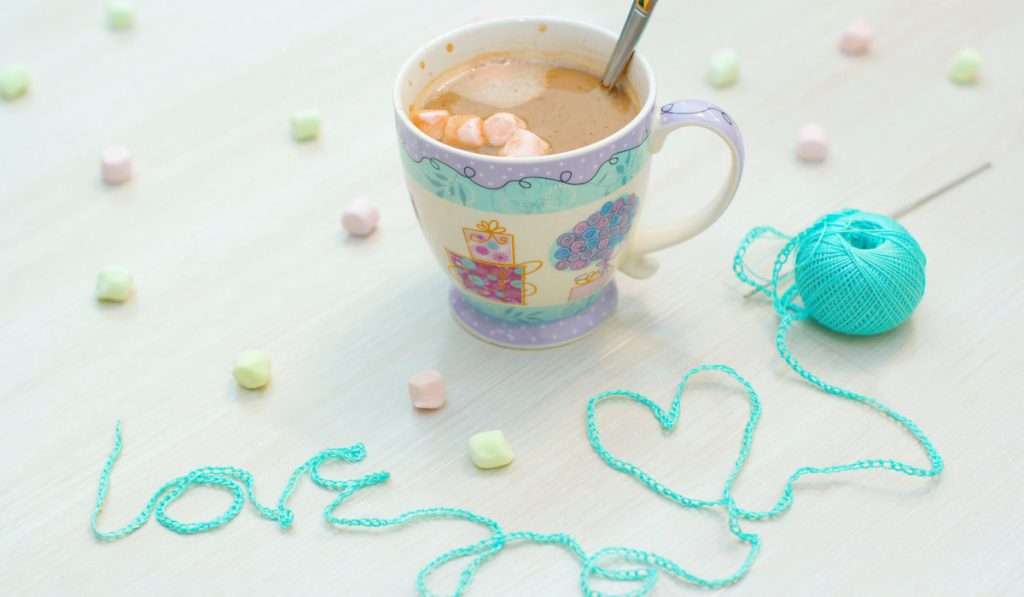 crochet, knit the word-love light blue yarn and cup of coffee on white background