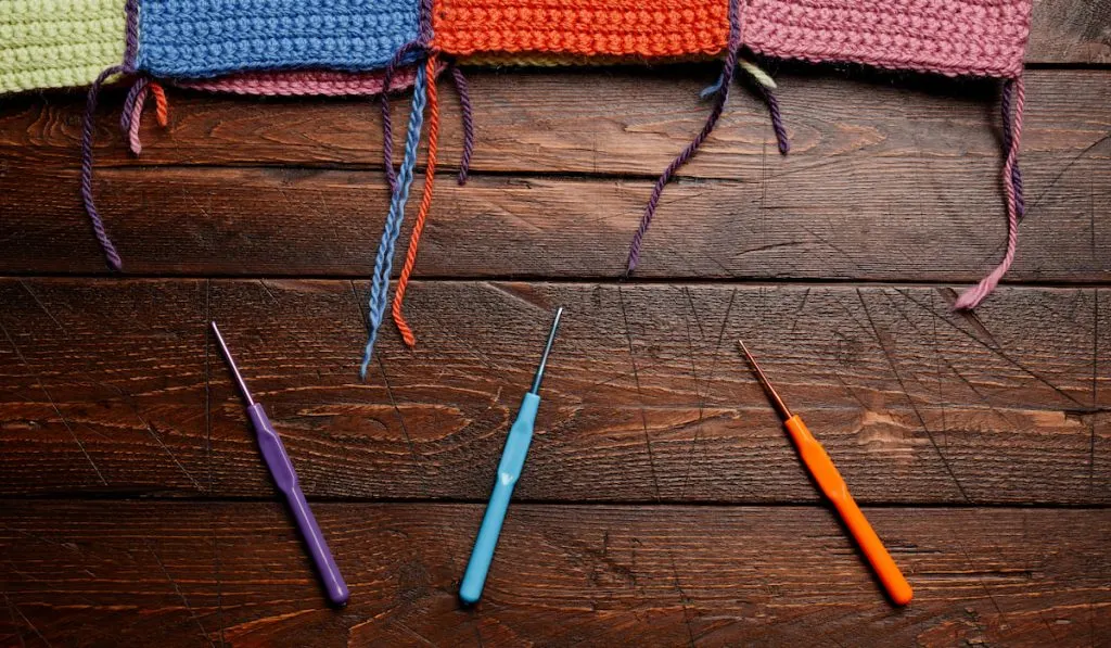 different colors of knitted yarn and crochet hooks on wooden table