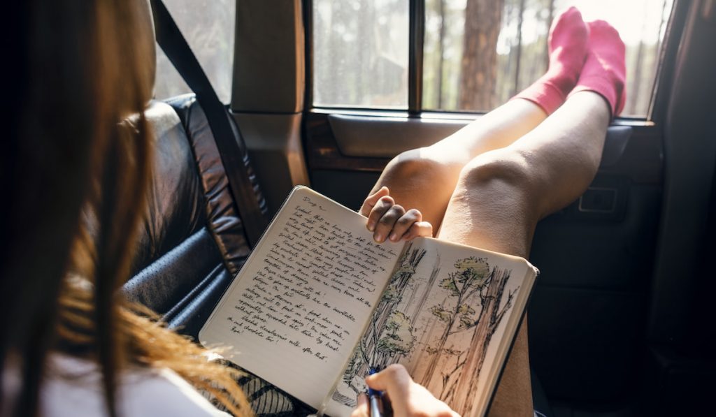 girl drawing on her journal while inside the car 