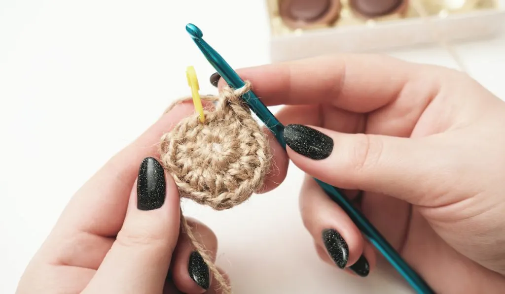 hands of a woman holding crochet and jute thread and fragment of a knitted pattern.