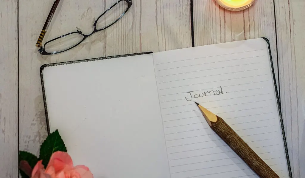 journaling open journal with flower candle and glasses on the table