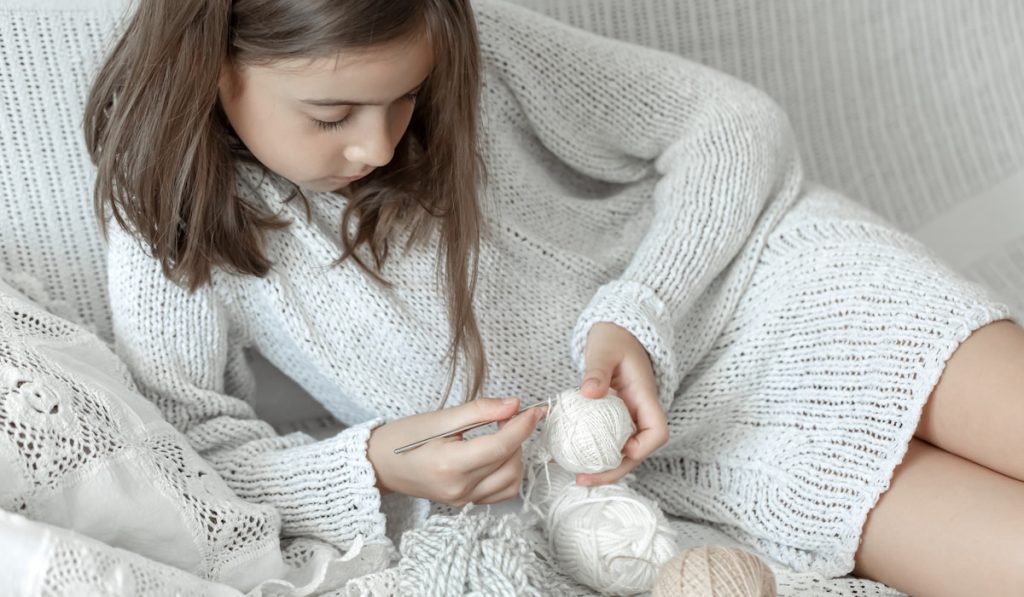 little girl at home on the couch learns to crochet