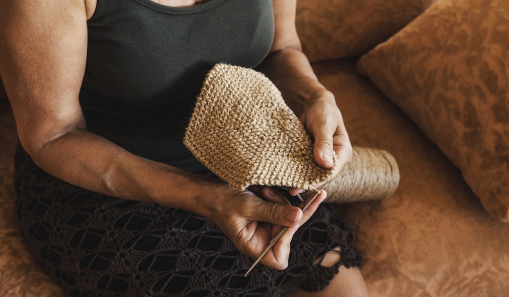woman crochets a napkin with natural thread inside in her living room. 