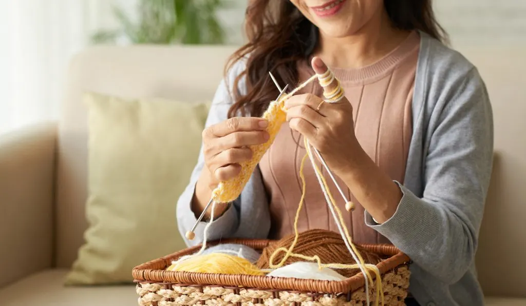 woman knitting yellow yarn with different color of yarns in the wooden basket 