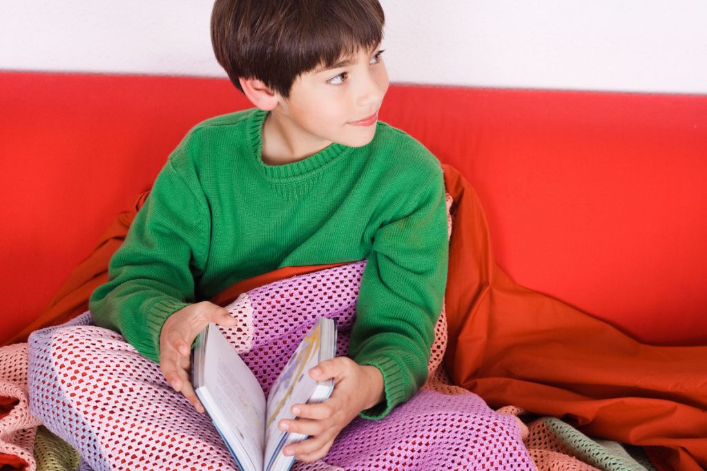 Child reading on a couch with blanket made of colorful yarns