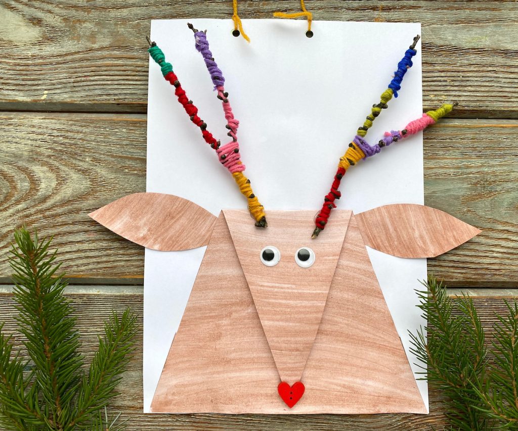 Children's application, creation of a cartoon animal similar to a deer on a paper and yarn on wooden table