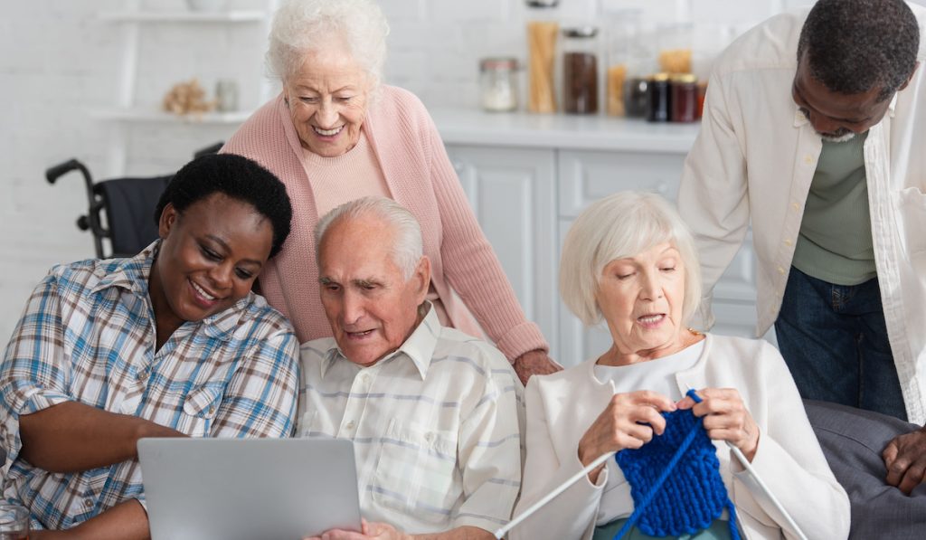 Men and women seniors spending time with yarn and laptop in nursing home