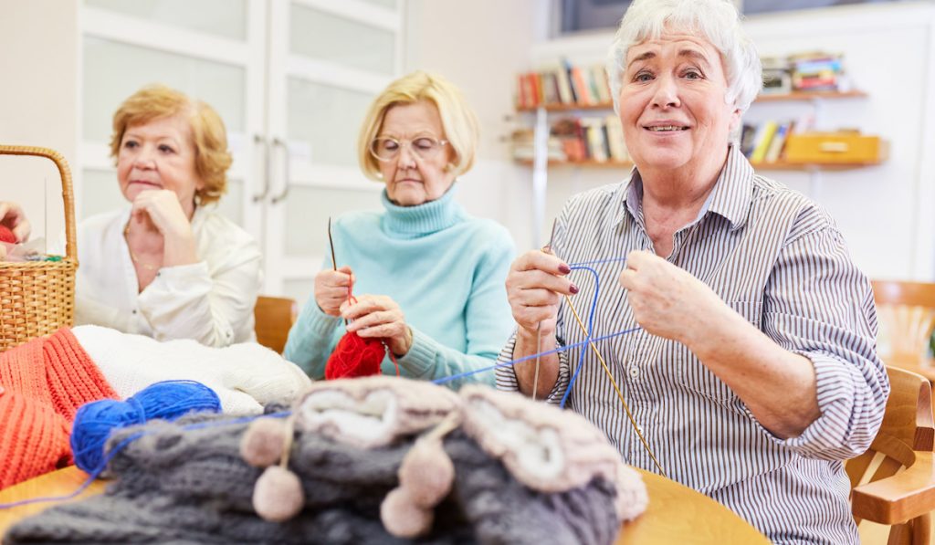 Three senior women crocheting and knitting as occupational therapy in a retirement home