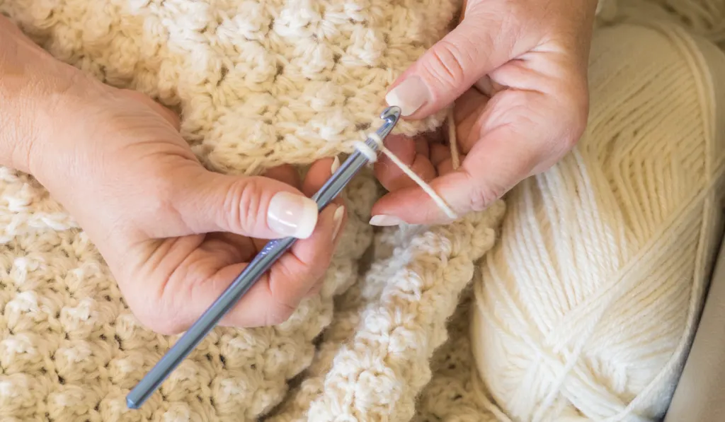 woman crocheting a cozy warm blanket  in a neutral color 