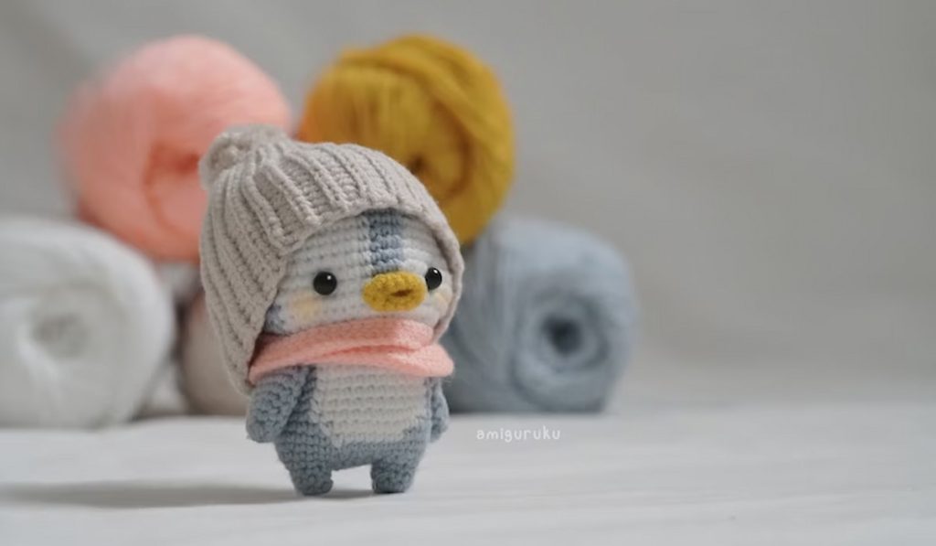 Crochet Pattern of the Lost Baby Penguin by Amiguruku with yarns in the background