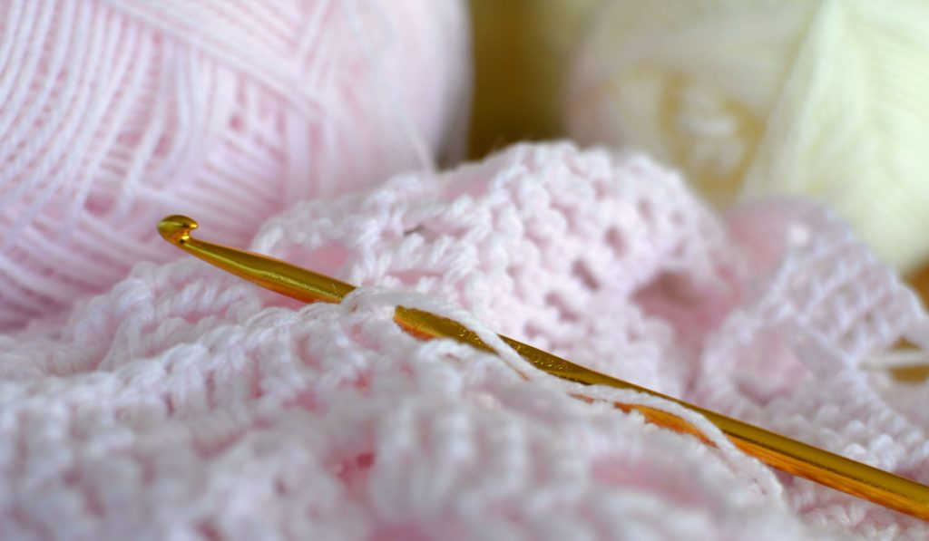 Crocheting a baby blanket with pastel pink yarn, crochet hook,