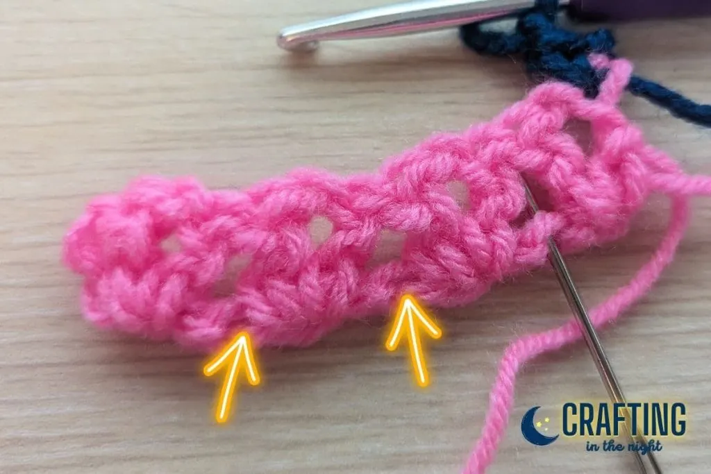 crochet swatch with a yarn needle showing the placement of the next stitch and yellow arrows showing the placement of the following two stitches