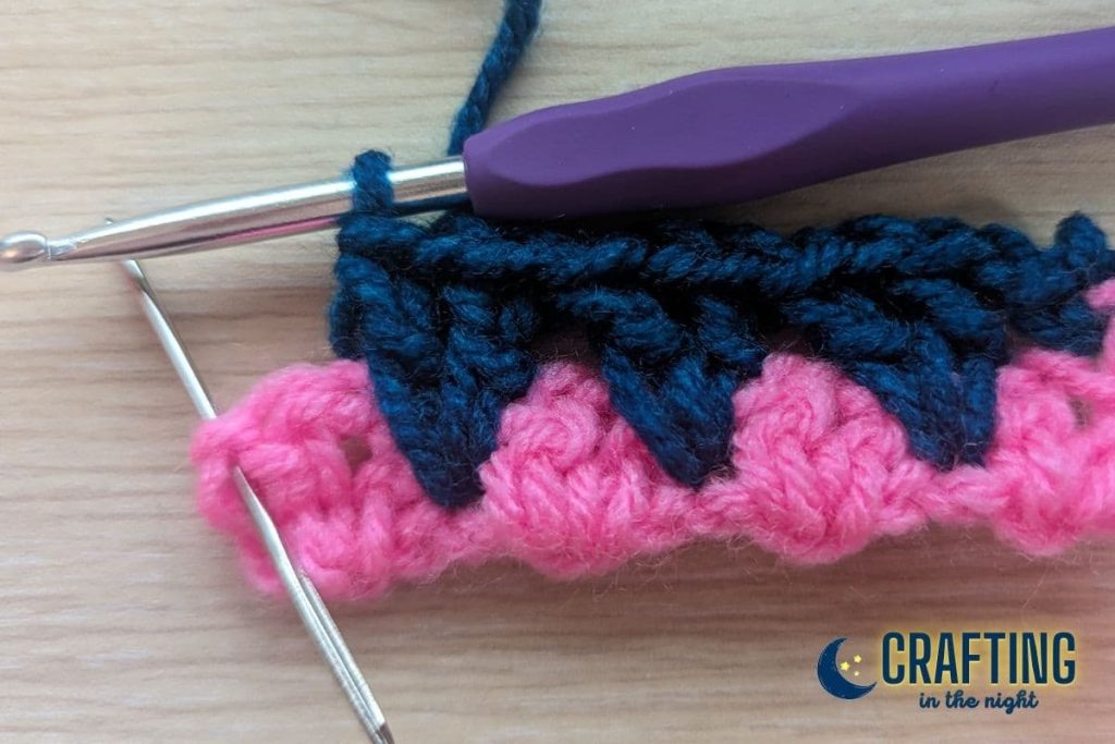 a crochet swatch where a yarn needle is placed in the last stitch to indicate where the last stitch of the row should be placed