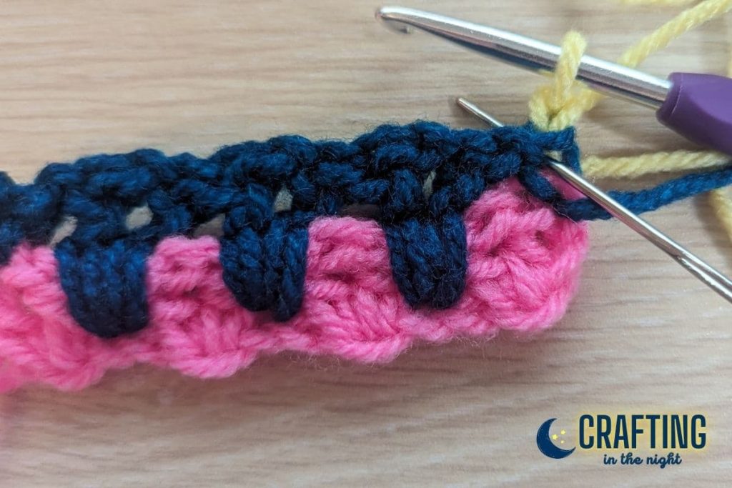 a crochet swatch with a yarn needle placed under the first stitch from the row below the current row indicating where the next single crochet should be placed