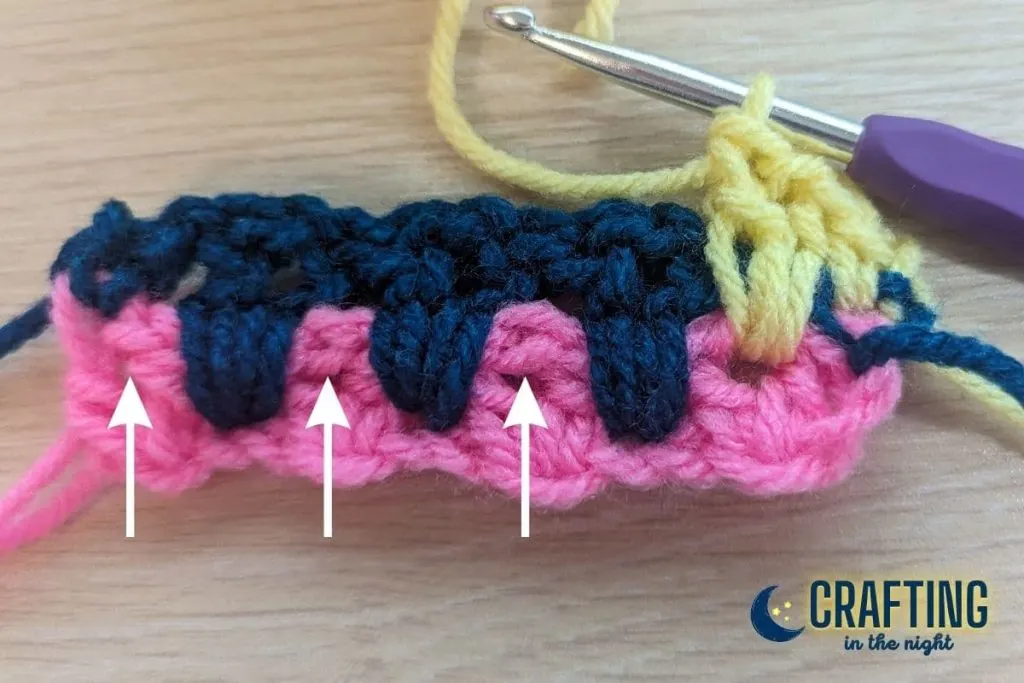 crochet swatch with arrows pointing where the next three v-stitches should ve placed.