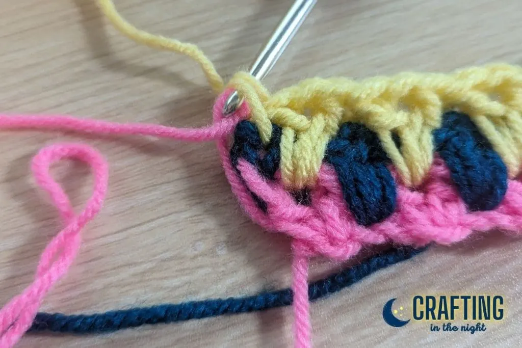 closeup of a crochet swatch where we are changing color from yellow to pink by carrying yarn up the side