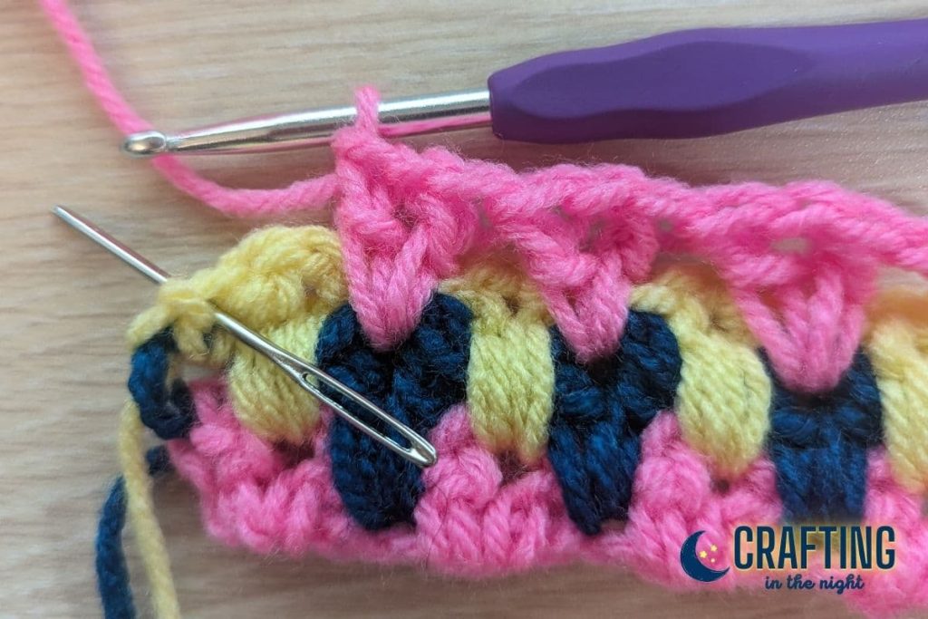 a crochet swatch with several v-stitches completed and a yarn needle indicating where the last stitch should be placed