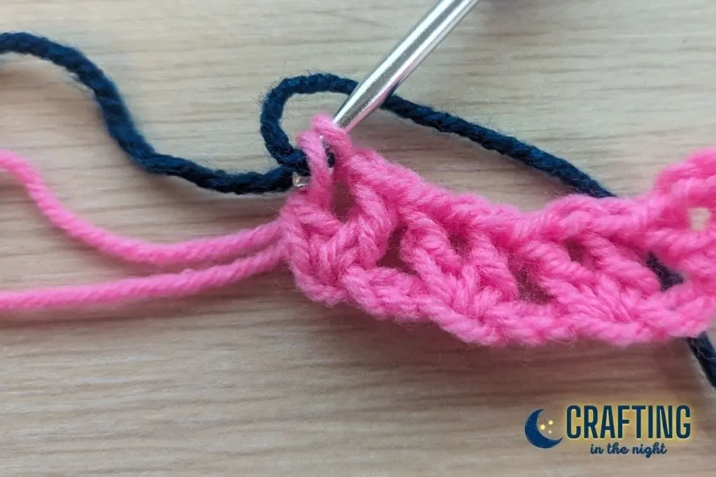 navy yarn being used to complete the last part of a double crochet from the pink row below