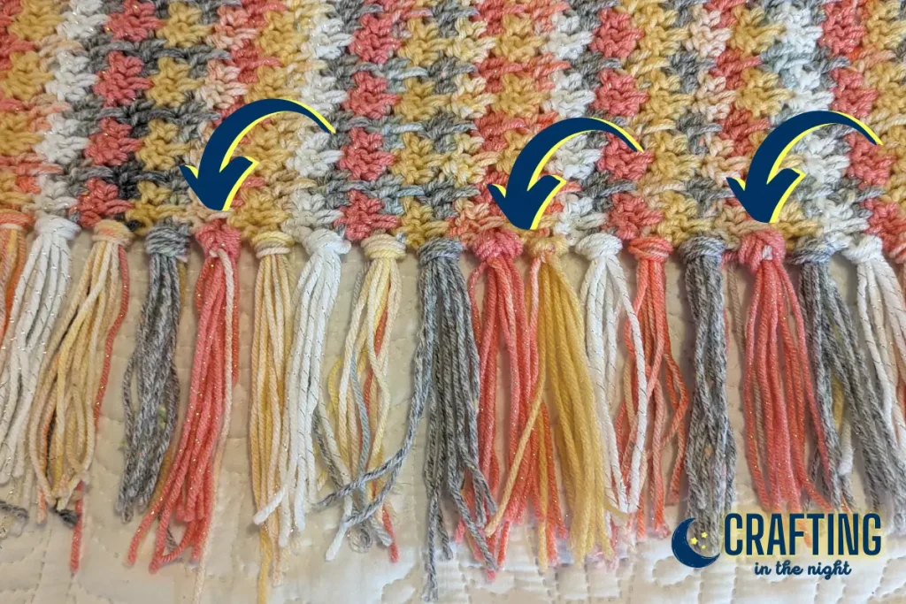 closeup of the tassels on a crochet blanket with navy arrows pointing to tassels that are facing the wrong direction