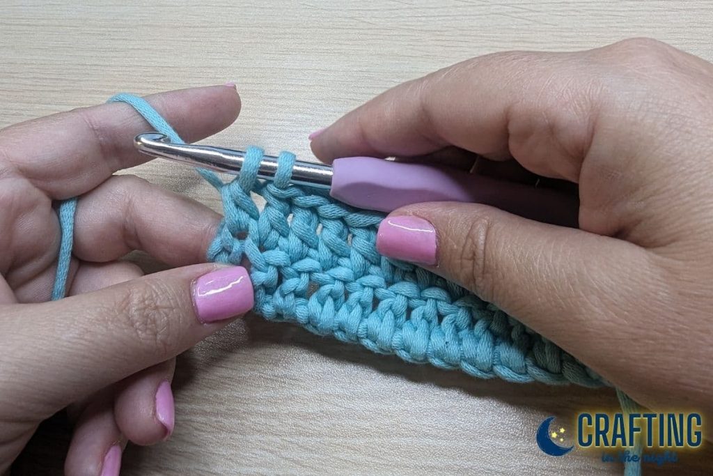 A double crochet of blue yarn and a metal crochet hook. Two loops left on the hook.