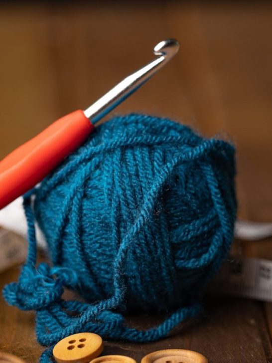 an ergonomic crochet hook leaning on top of a blue yarn ball
