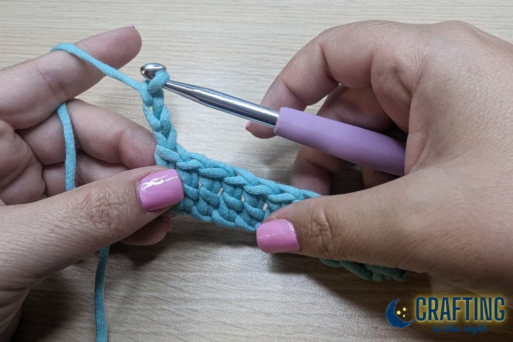 A chain of blue yarn held between two hands. Turning in double crochet. Create three chain and the third chain is your turning chain.